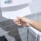 Mano retirando una toalla intercalada del dispenser montado en la pared.