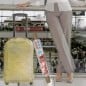Valija amarilla envuelta en film stretch transparente en un aeropuerto, junto al rollo con mango