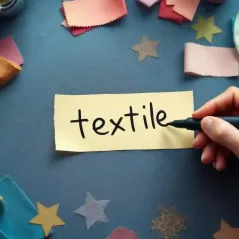 Rótulo escrito con marcador sobre una tira de cinta de papel, en una mesa con telas y carreteles