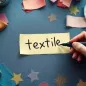 Rótulo escrito con marcador sobre una tira de cinta de papel, en una mesa con telas y carreteles