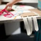 Tiras de cinta de papel colgando del borde de una mesa de manualidades con cartón y recortes