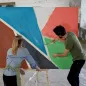 Dos personas pintando un mural geométrico y retirando la cinta de papel que enmascaró los bordes de cada color Dos personas pintando un mural geométrico y retirando la cinta de papel que enmascaró los bordes de cada color