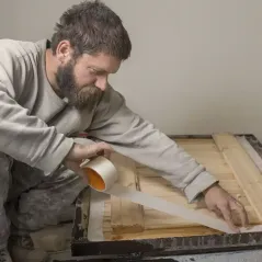 Hombre colocando cinta de papel ancha sobre el borde de un marco de madera para protegerlo antes de pintar